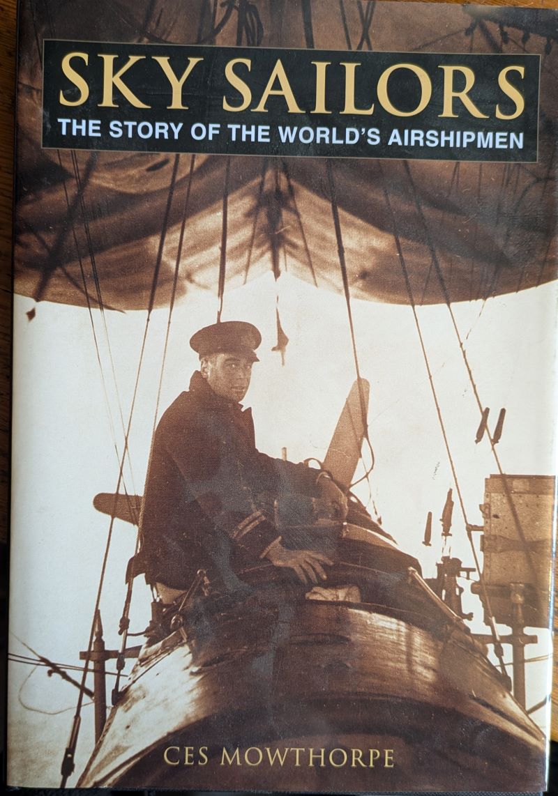 Picture of book cover showing uniformed airship pilot airborne and sitting outside behind the propellor with the airship envelope above his head